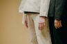 A minimalist fashion image showing models in long-sleeve outfits against a beige background.
