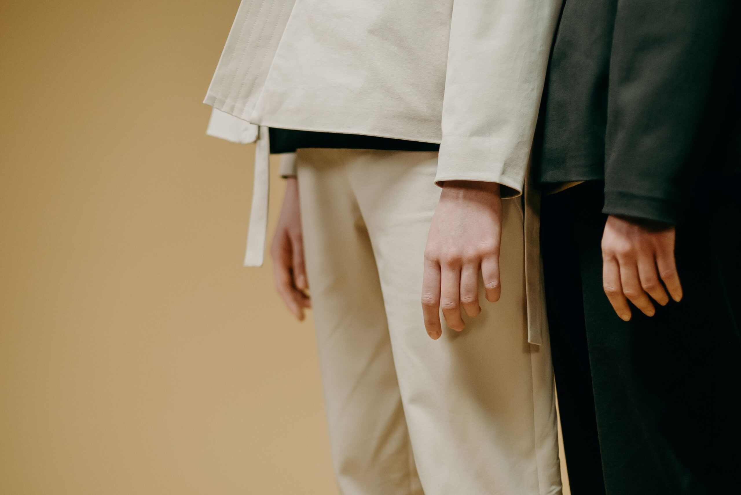 A minimalist fashion image showing models in long-sleeve outfits against a beige background.